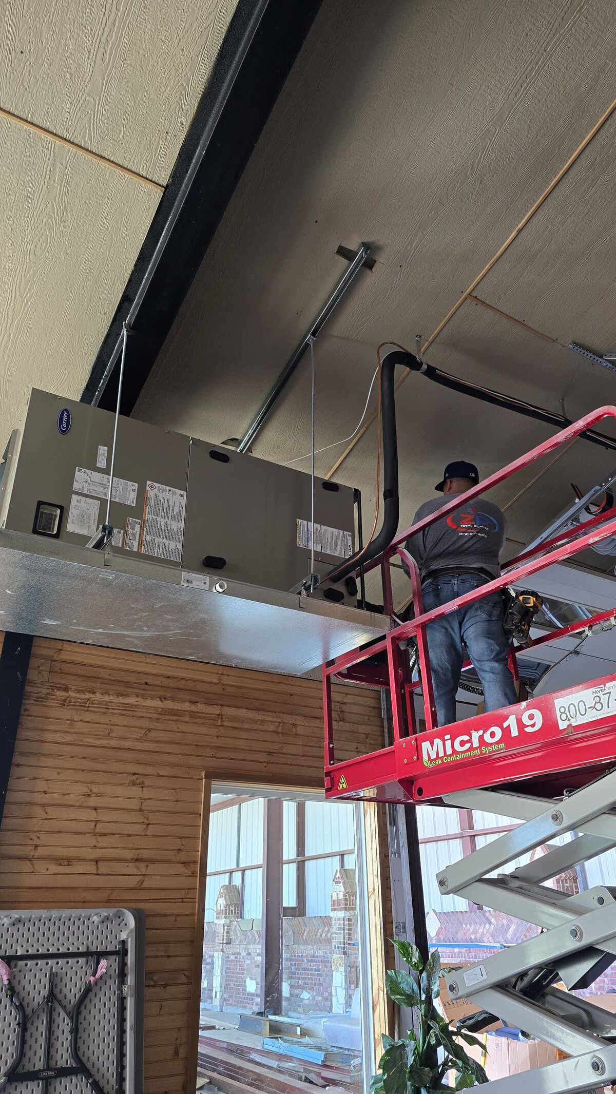 Technician on a scissor lift working at an overhead air handler inside a commercial building