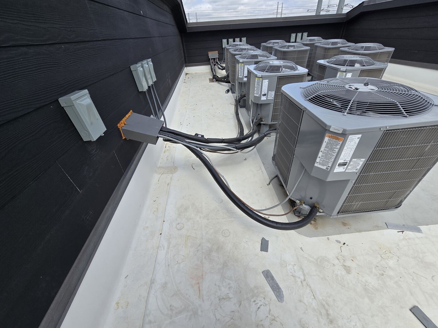 Condensing units lined up along a commercial building wall with electrical disconnects above them