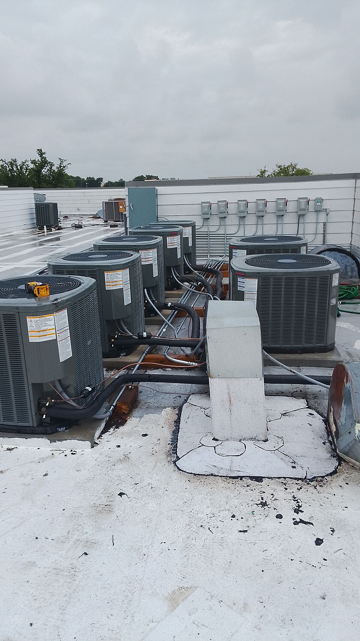 Row of condensing units set on curbs across a flat white commercial roof