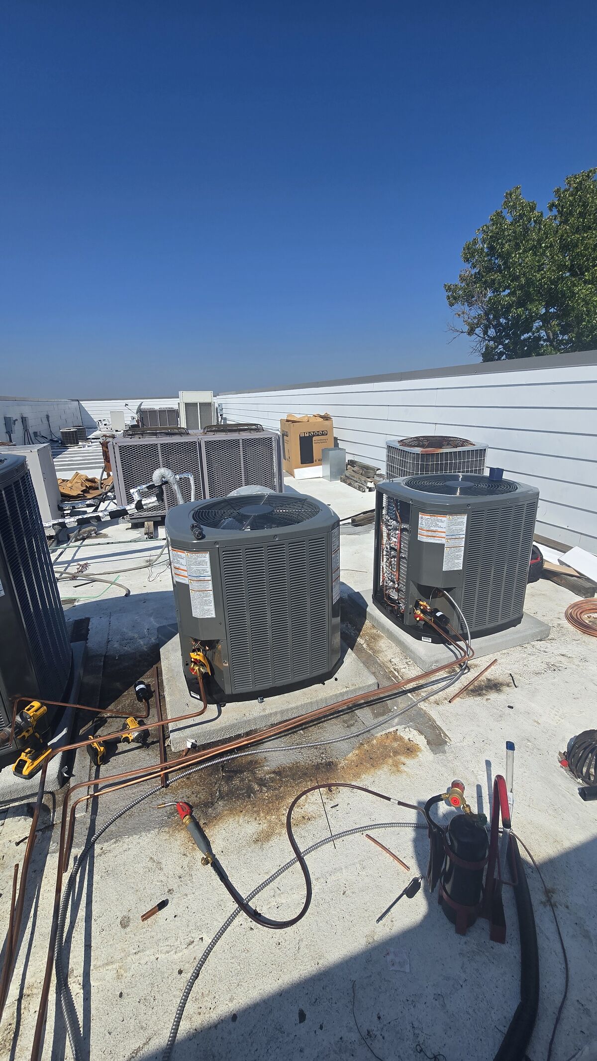 Two rooftop condensers with copper line sets and hand tools laid out on the roof